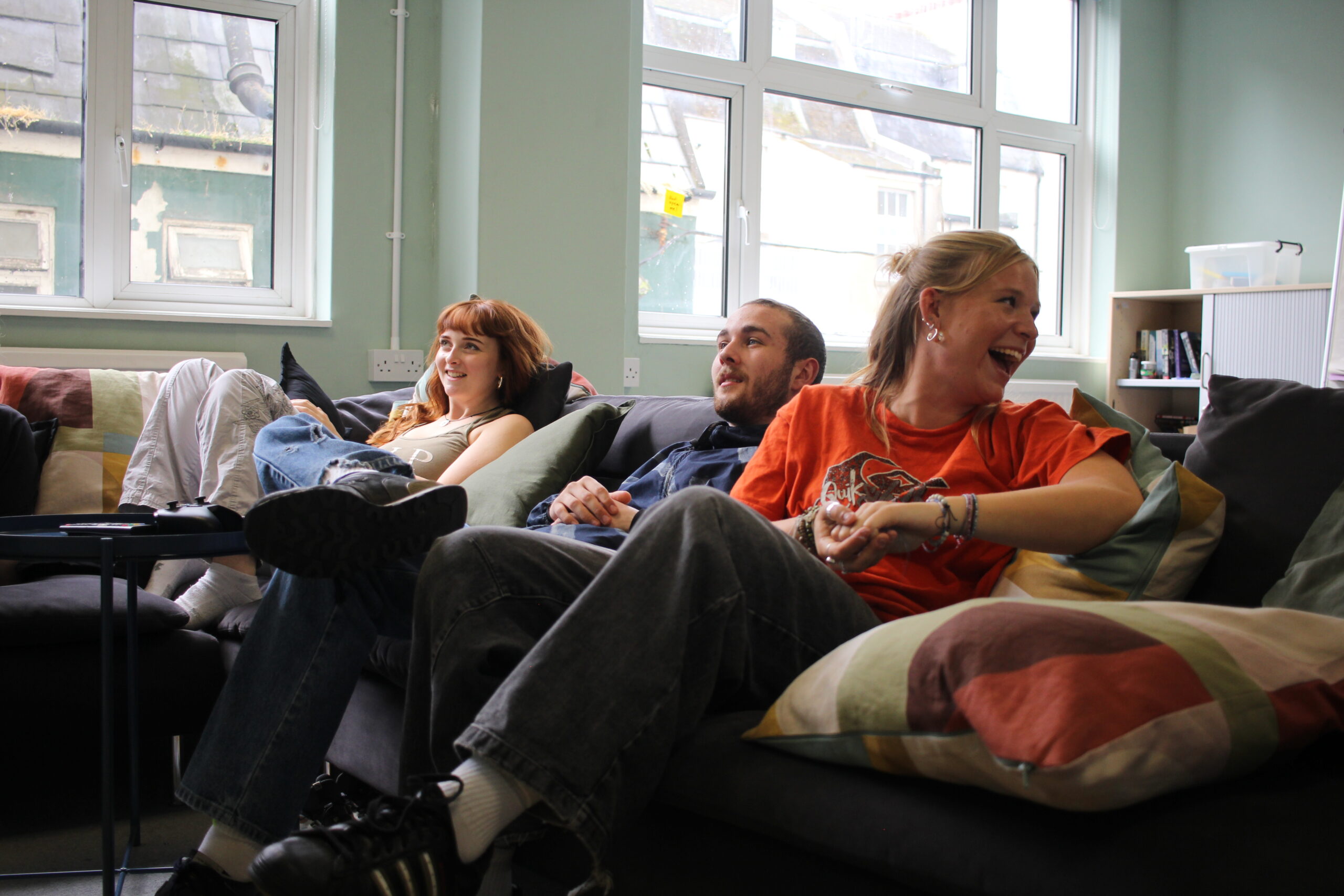 Young people laughing and playing video games on a couch in our day centre